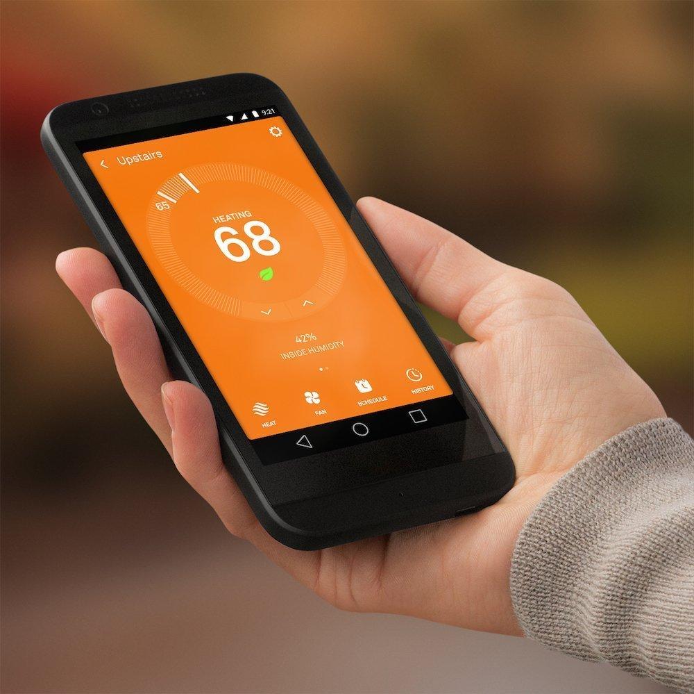 Hand holding a smartphone displaying an orange heating control app interface, showing the number 68.