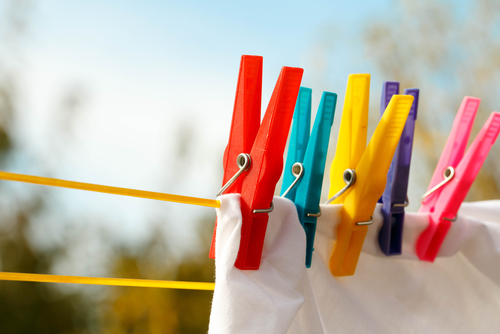Brightly colored clothespins on a yellow clothesline holding a white fabric.